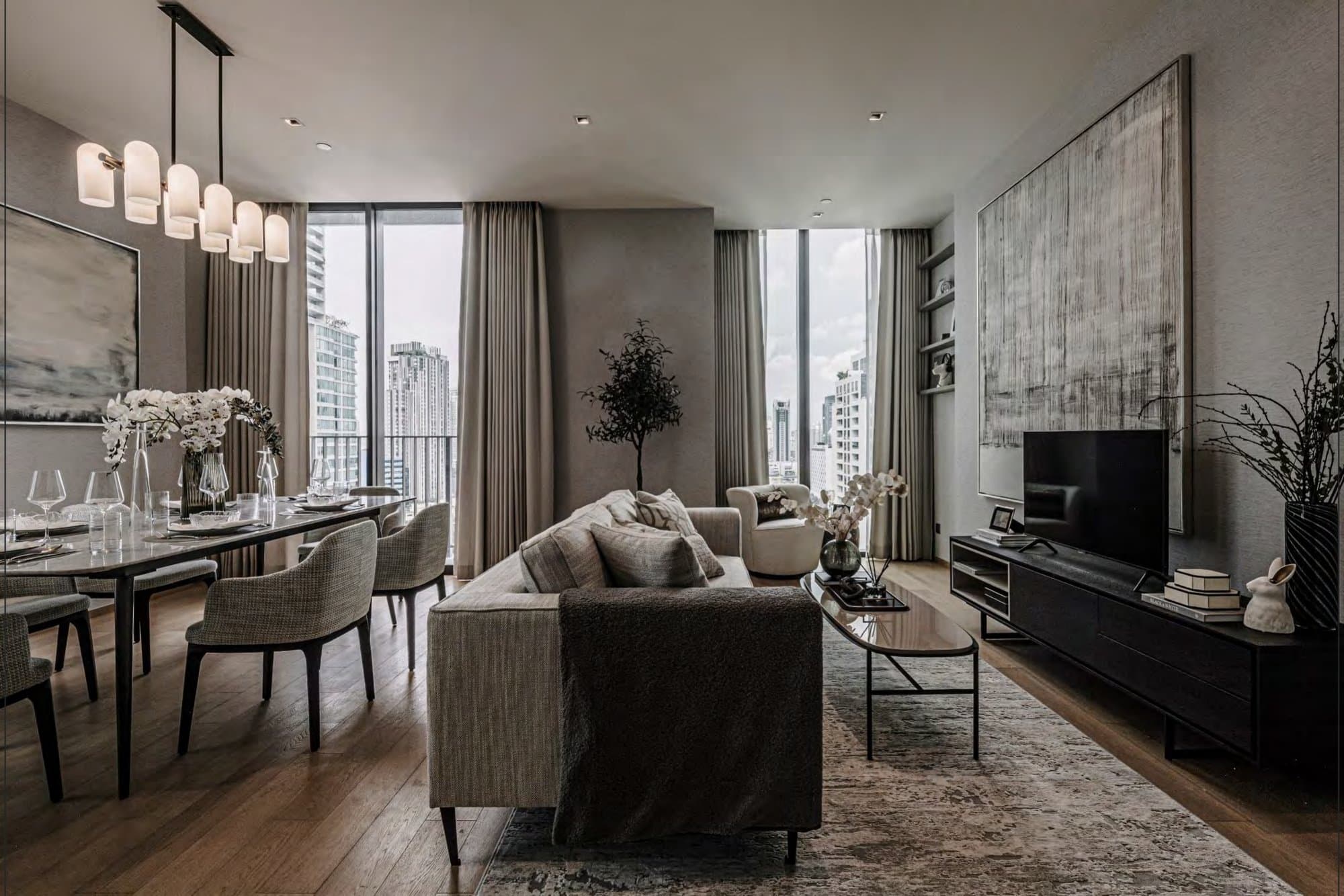 Warm-toned living room with grey sofa, black media console and a large textured abstract canvas, dining table alongside and city towers through the glass