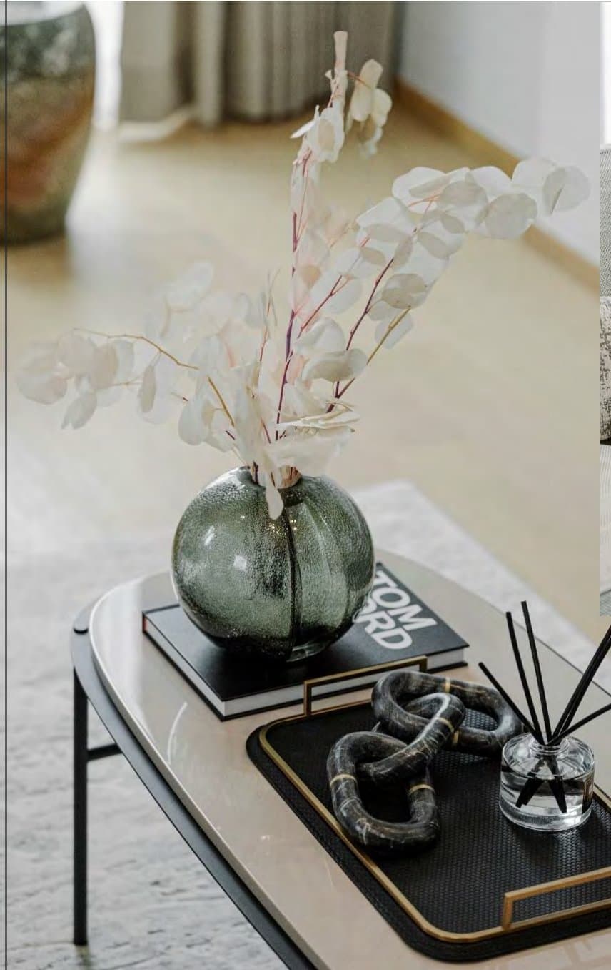 Coffee-table detail with a smoky glass vase of white eucalyptus, stacked design books, a marble chain-link object and a reed diffuser