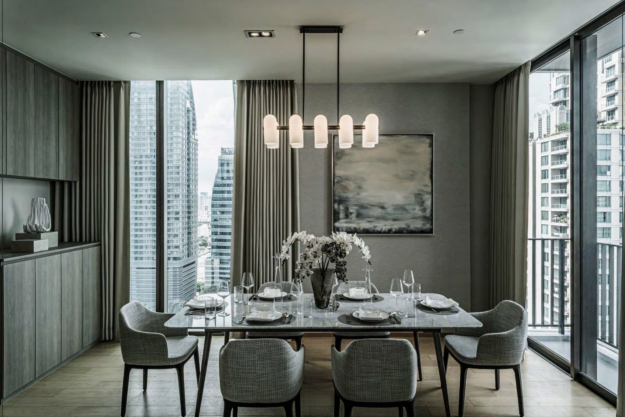Dining room with marble-top table, woven grey armchairs, opaline pendant and an orchid centrepiece, high-rise towers filling the tall windows