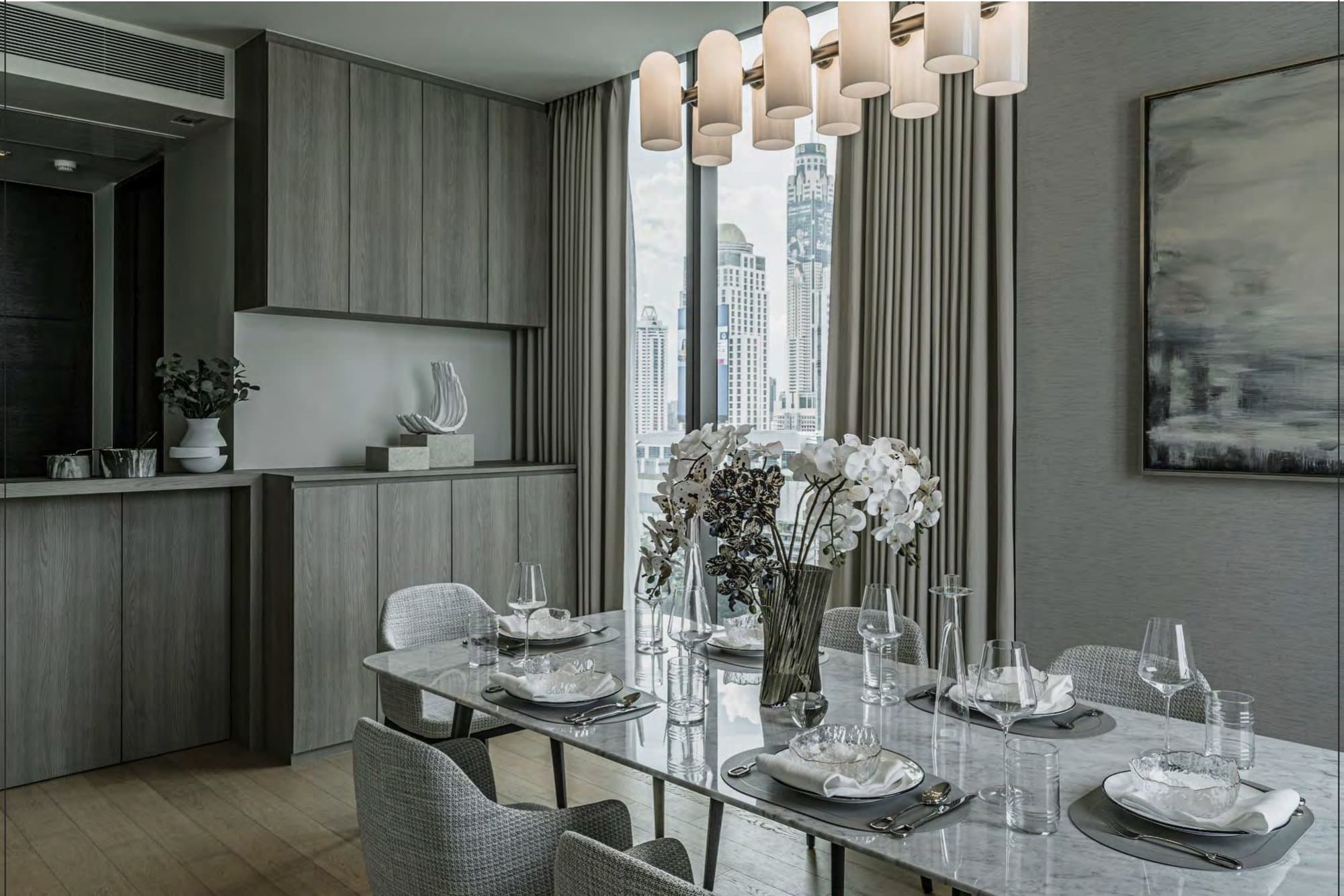 Dining table dressed with white and speckled orchids, glassware and slate chargers, pale oak joinery behind and skyline through sheer-draped glazing