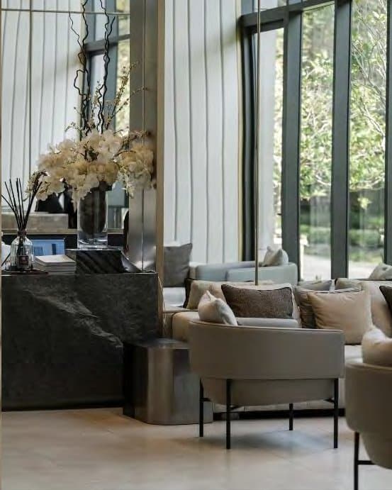 Corner lounge vignette with white orchids on a dark marble console, a cream tub chair and sofa beside garden-view glazing.