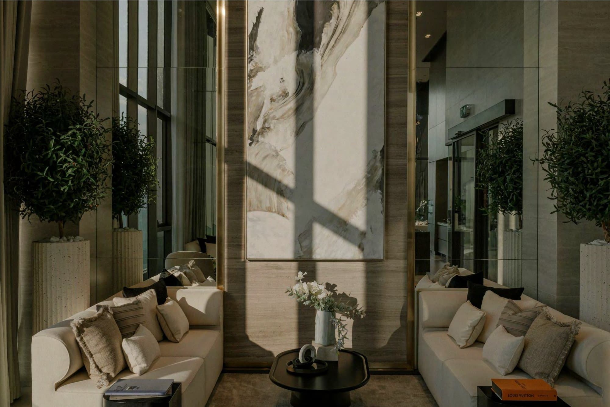 Twin cream sofas face a tall abstract canvas between mirrored panels, flanked by olive topiaries in fluted stone planters.