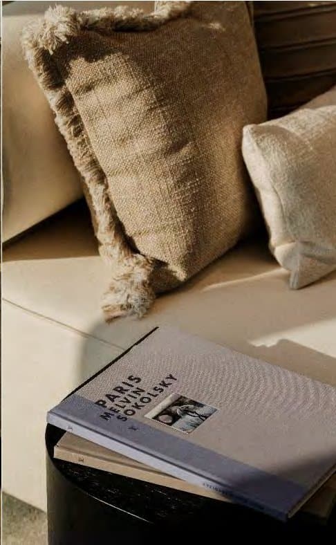 Close styling detail of a fringed jute cushion and soft bouclé against a cream sofa, with a grey art book resting nearby.