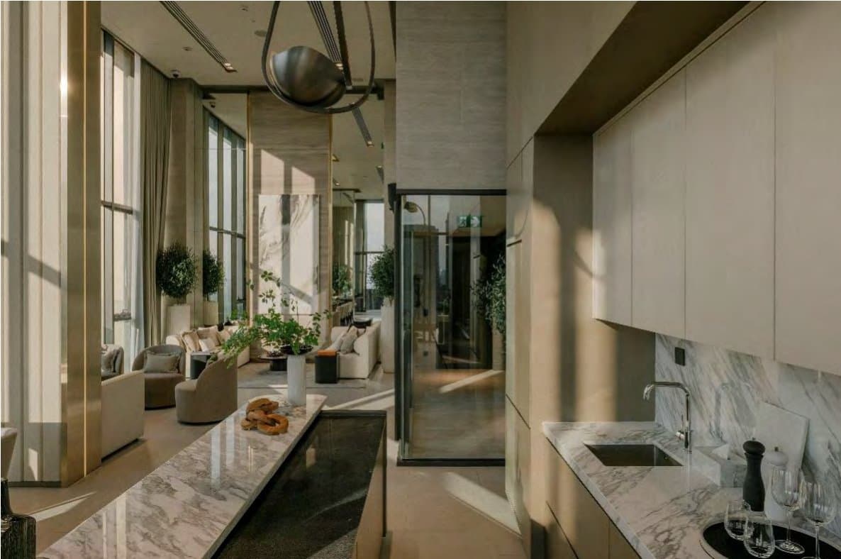 Pantry with a veined white-marble waterfall counter and undermount sink, opening back toward the sunlit lounge and full-height windows.