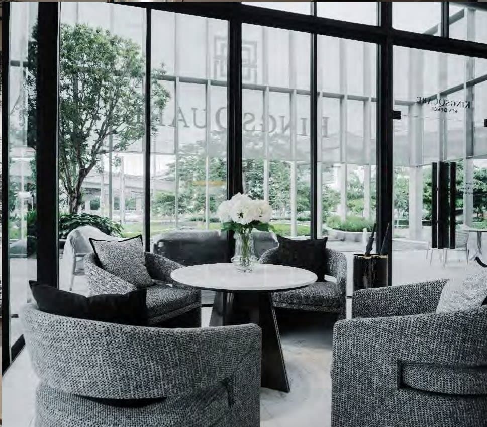 Grey bouclé tub chairs around a small marble table beside floor-to-ceiling glazing, white hydrangeas and a leafy garden outside.