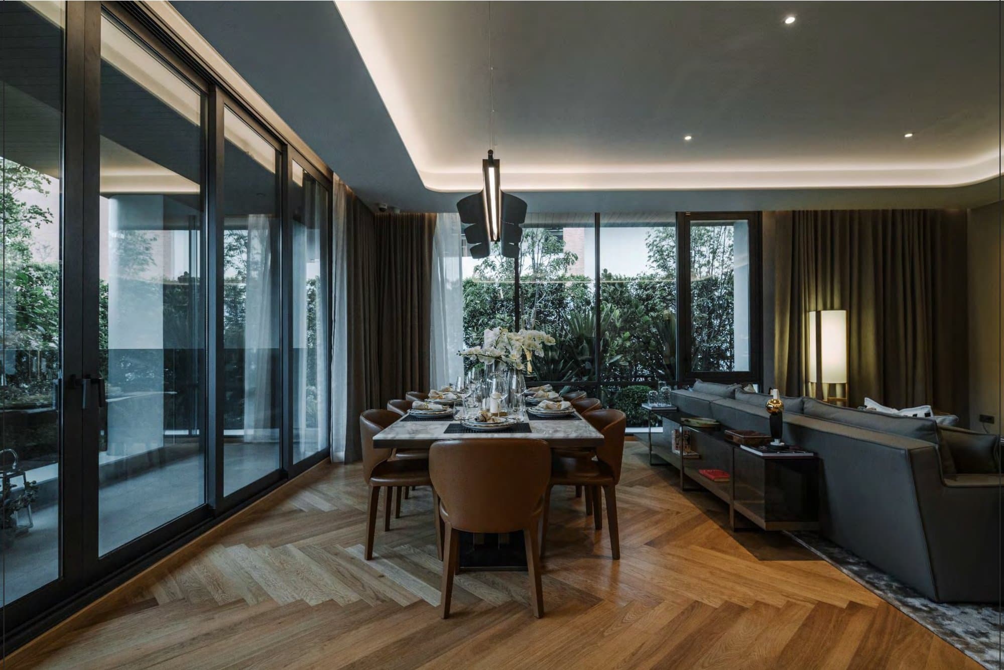 Dining room with a marble-topped table, tan leather chairs, sculptural pendant and herringbone oak floor beside a wall of glass.