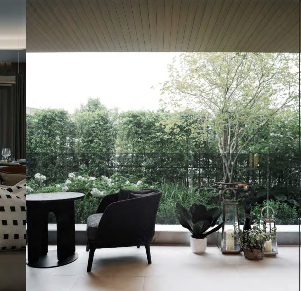 Sheltered terrace with a black armchair, round stone side table, potted greenery and glass balustrade opening to garden trees.
