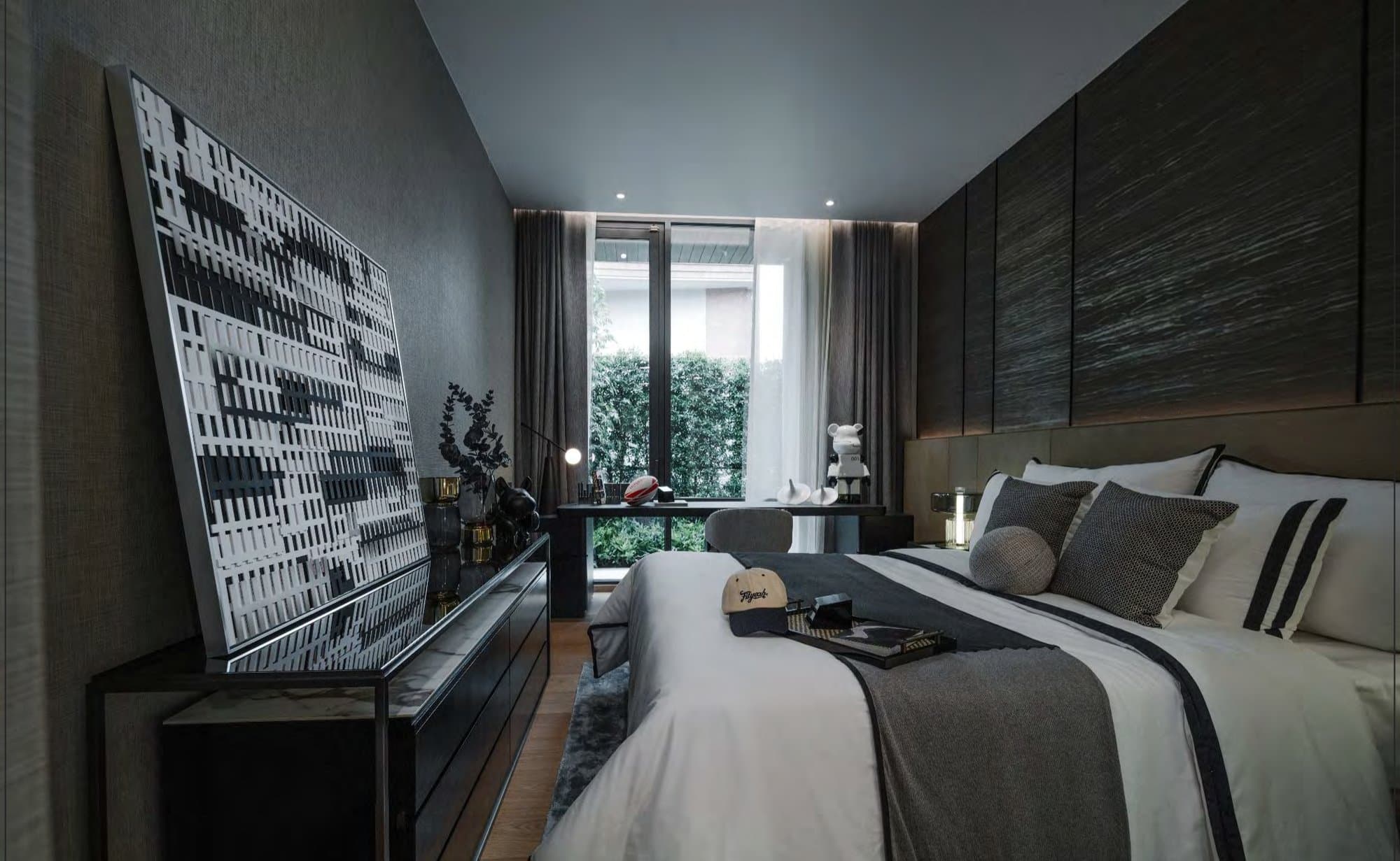 Bedroom with a large black-and-white artwork, dark timber headboard wall, layered grey linens and garden view through sheer curtains.