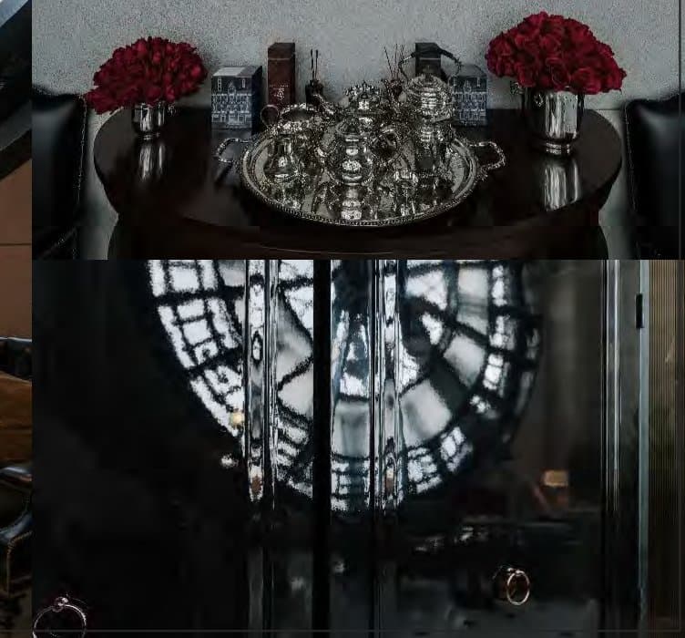 Dark round console set with an antique silver tea service and red roses, the clock face reflected in glossy black cabinetry below.