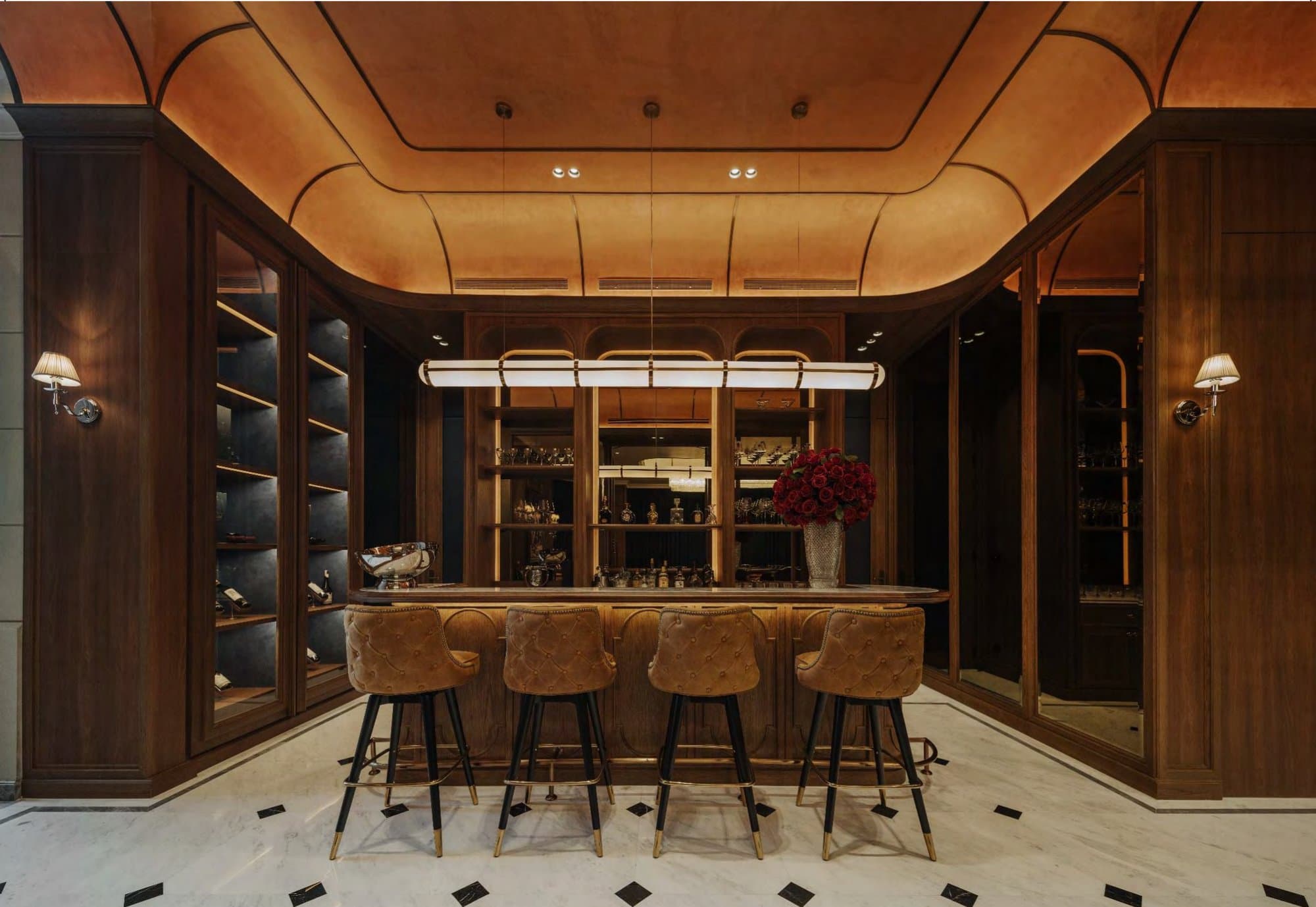 Walnut home bar with backlit bottle shelving, tan buttoned leather stools and a curving leather-clad ceiling glowing amber overhead.