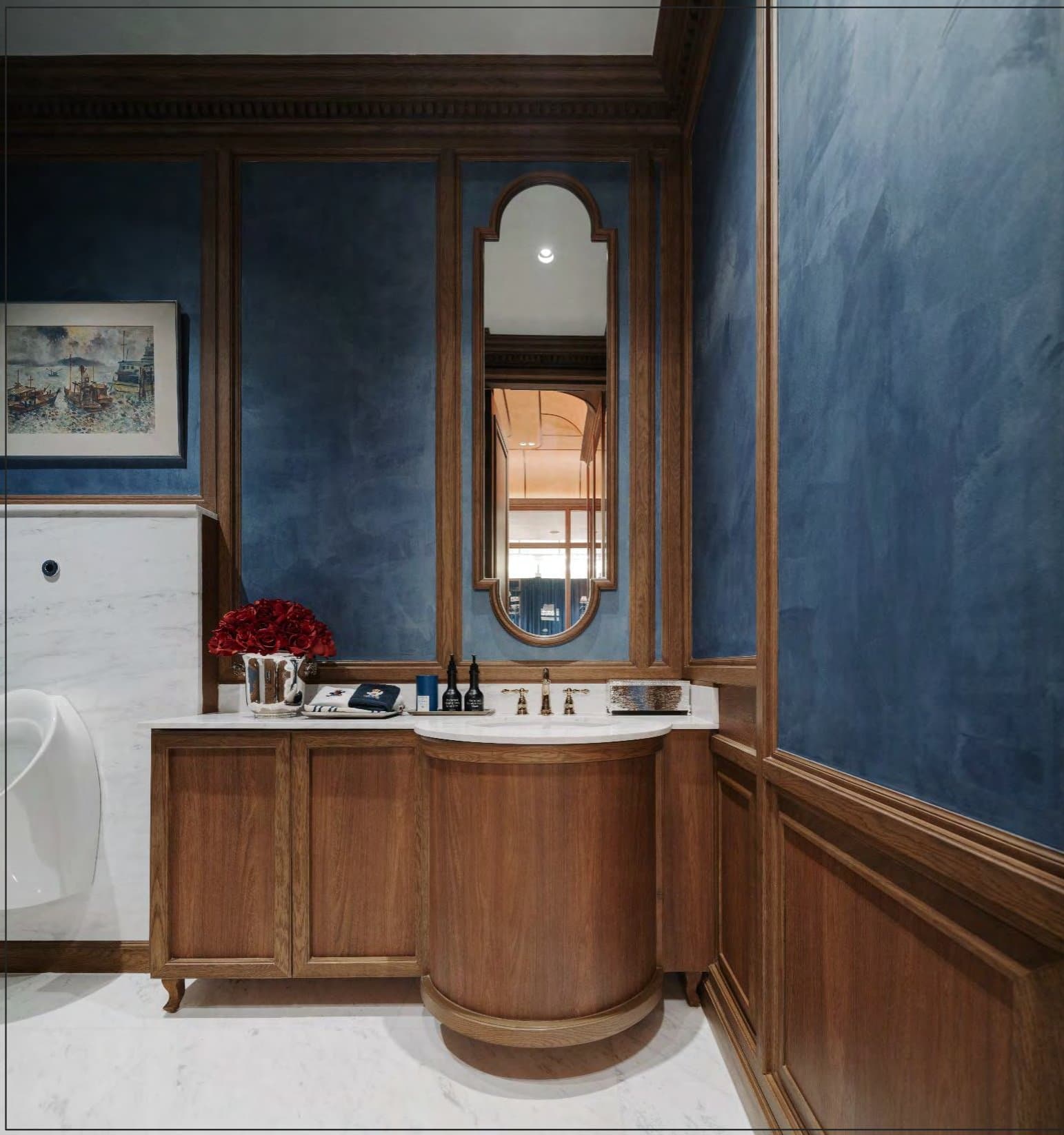 Powder room walled in hand-trowelled blue plaster, a curved oak vanity with marble top, arched mirror and small maritime watercolour.