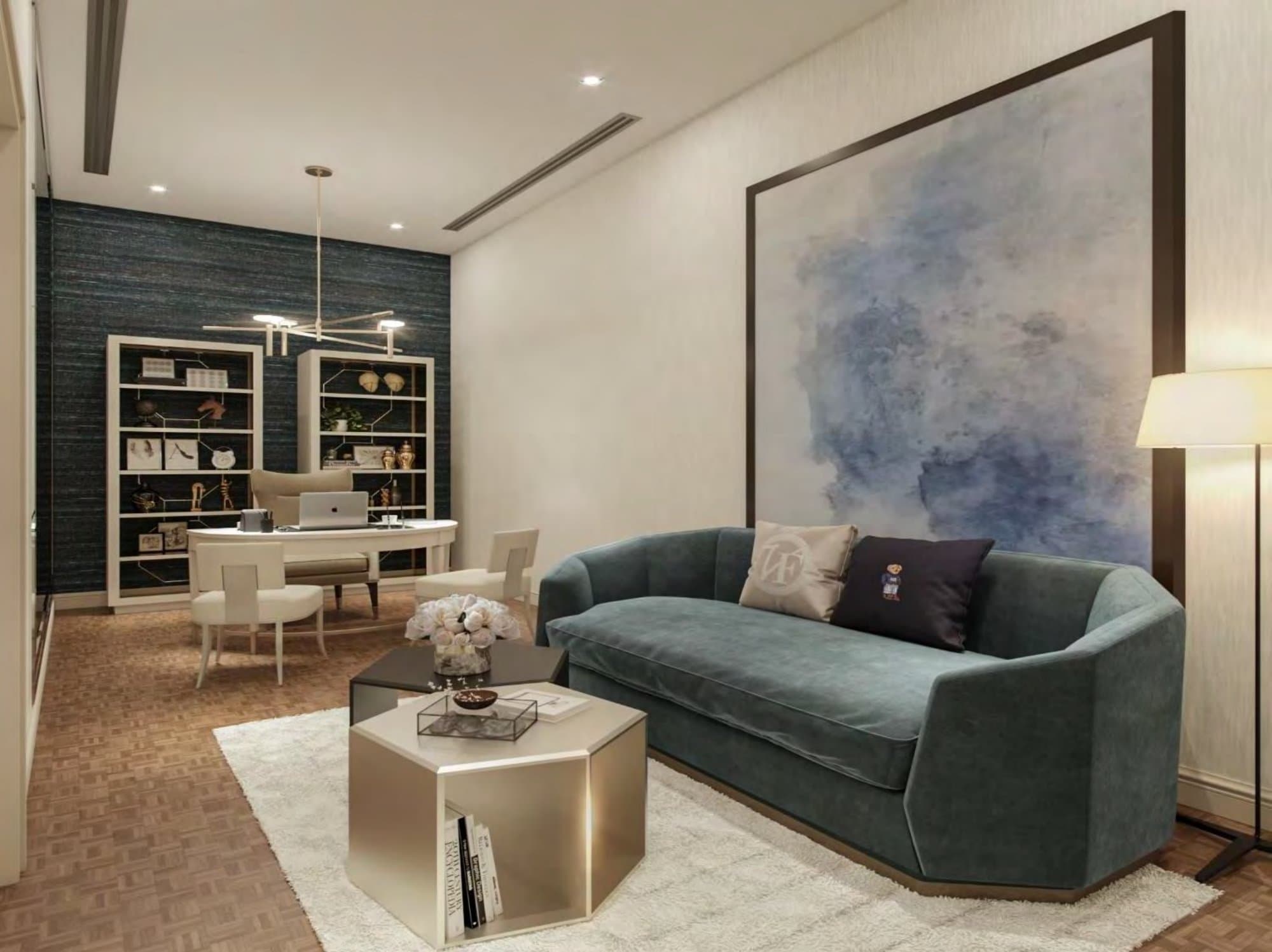 Study corner with teal velvet sofa beneath a soft blue abstract canvas, white lacquer desk and glazed bookcases against dark grasscloth walls.