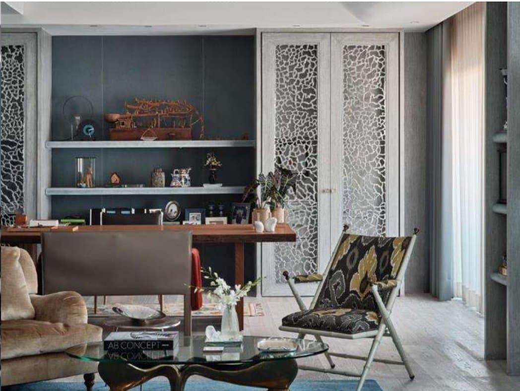 Study corner with a timber writing desk, charcoal display niche, ikat-upholstered folding chair and pierced-lattice doors beside a glass cocktail table.