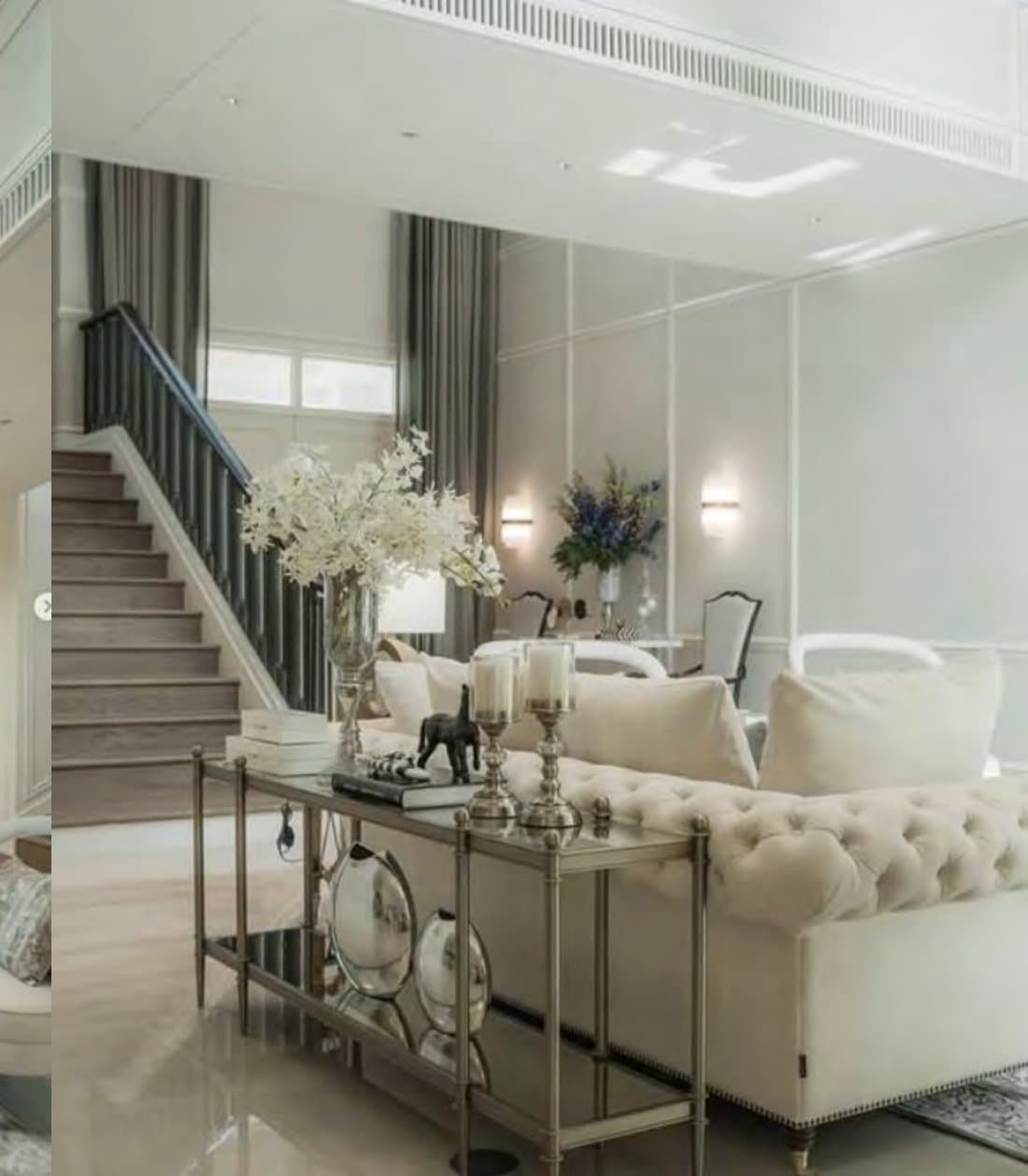 Entry vignette by a pale timber staircase: a mirrored steel console styled with silver candlesticks and white orchids beside a buttoned cream sofa