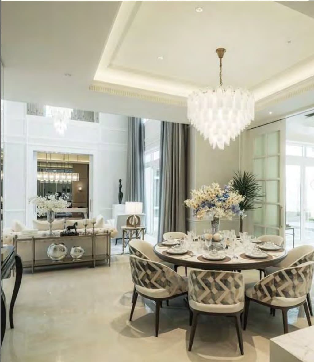 Dining room with a round timber table, chevron-patterned chairs and a tiered capiz chandelier, a mirrored sideboard and tall grey drapes beyond