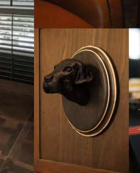 Close-up of a bronze retriever's head on a brass ring set into warm walnut joinery, shutters softly reflected behind