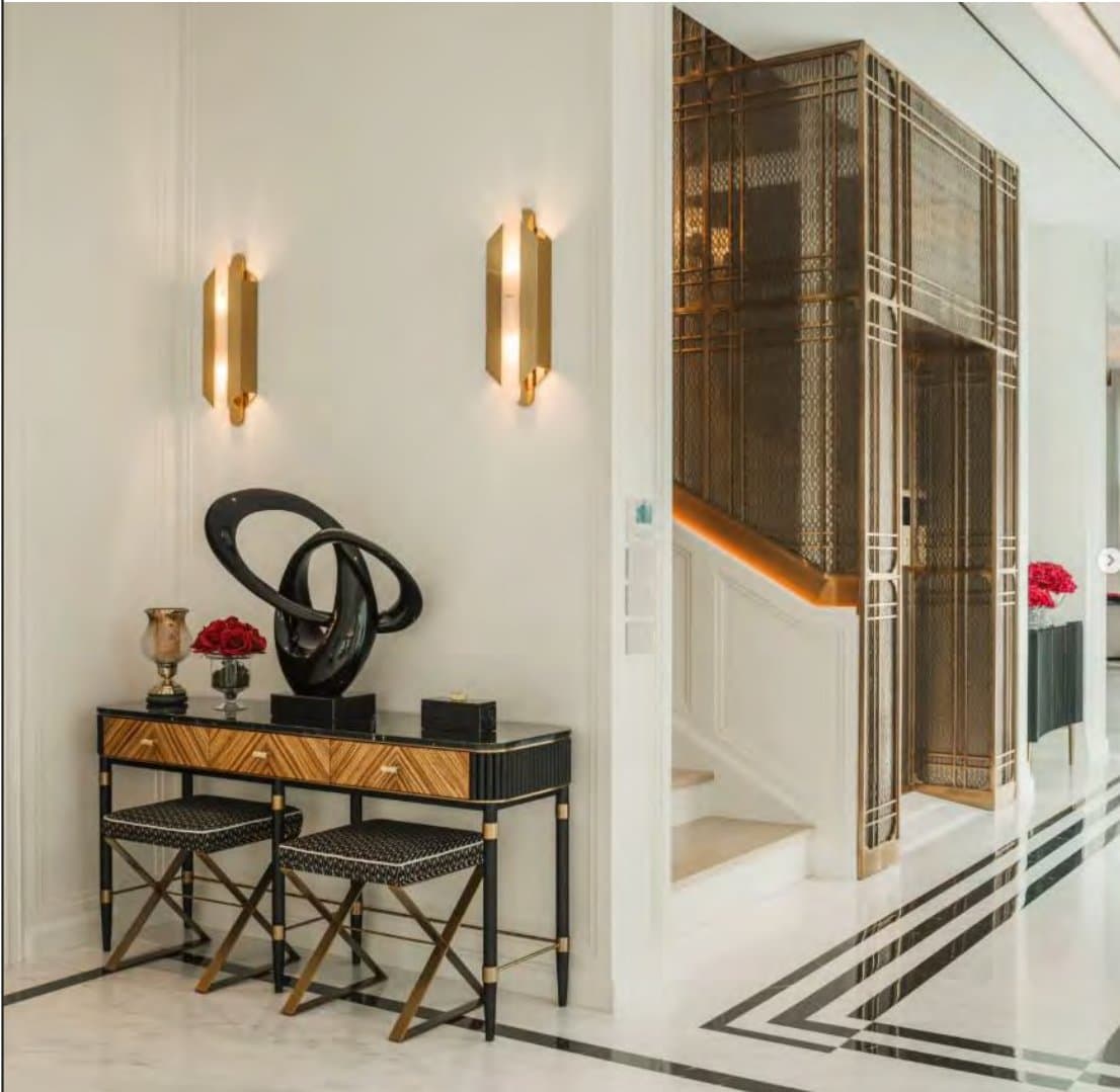 Entrance vignette with a black and zebra-wood console, twin brass sconces, a dark abstract sculpture and a brass screen enclosing the staircase.