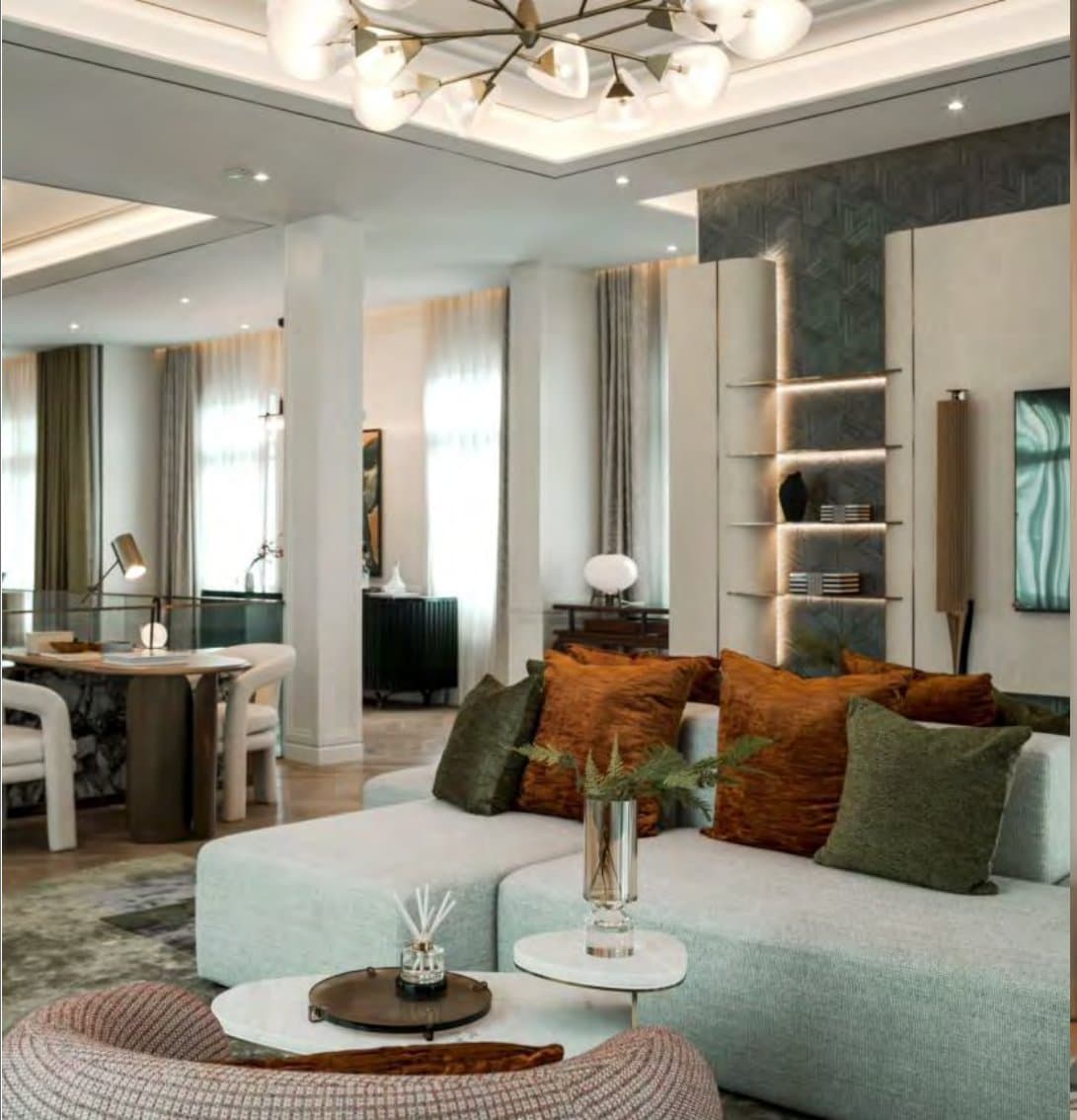Open family living room with a sea-green sectional, rust and moss velvet cushions, and a backlit niche set into a textured dark wall.