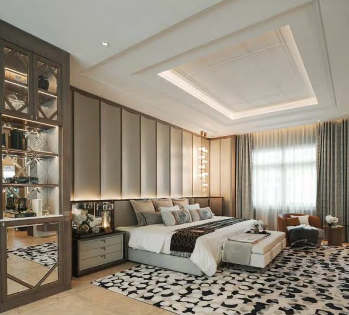 Master bedroom with a channel-panelled bed wall, tray ceiling in cove light, a mirrored display cabinet and a spotted monochrome rug.