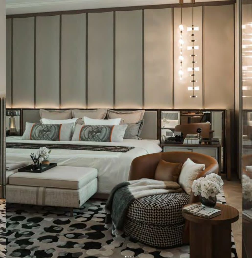 Master bedroom detail with an upholstered headboard, tan leather chaise, houndstooth ottoman, cascading bead pendants and a spotted black-and-white rug.