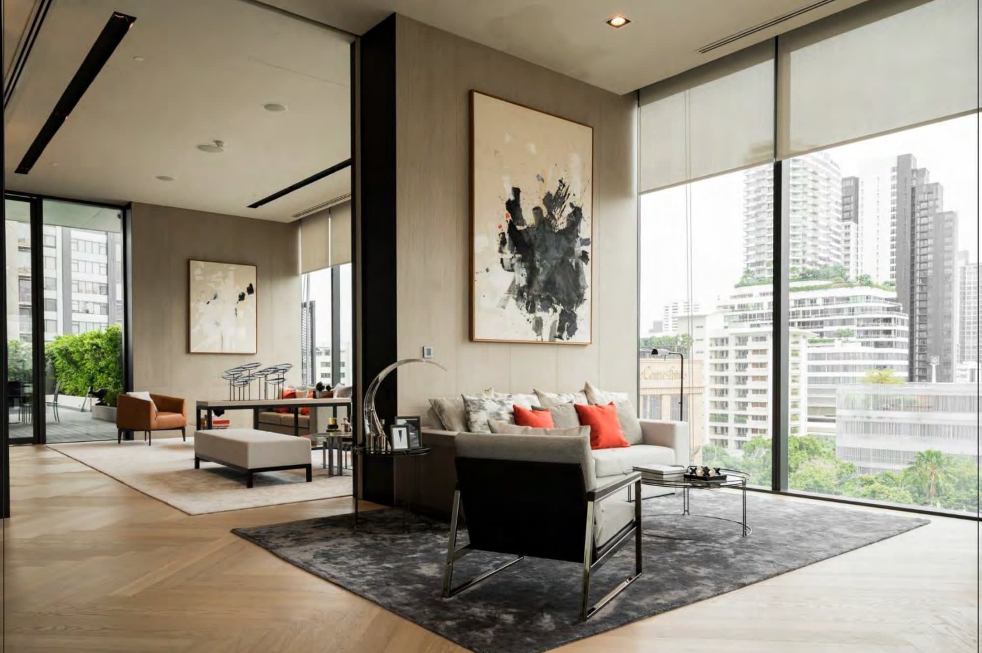 Double-height lounge with a bold black-ink canvas, oatmeal sofa dressed in coral cushions, and floor-to-ceiling windows framing Bangkok towers
