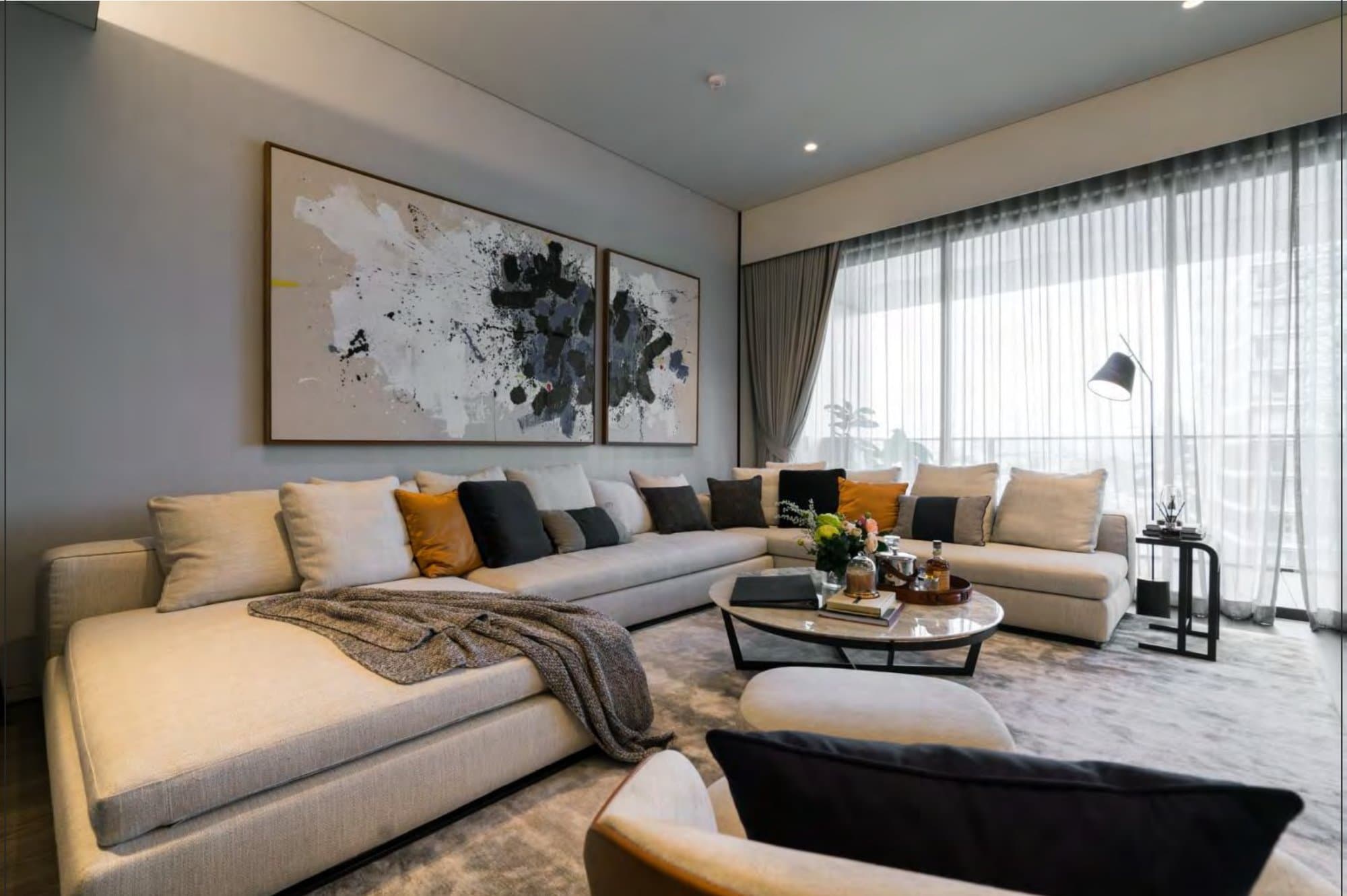 Calm living room with an L-shaped oatmeal sectional, black-and-white ink diptych, round marble coffee table and sheer-curtained windows