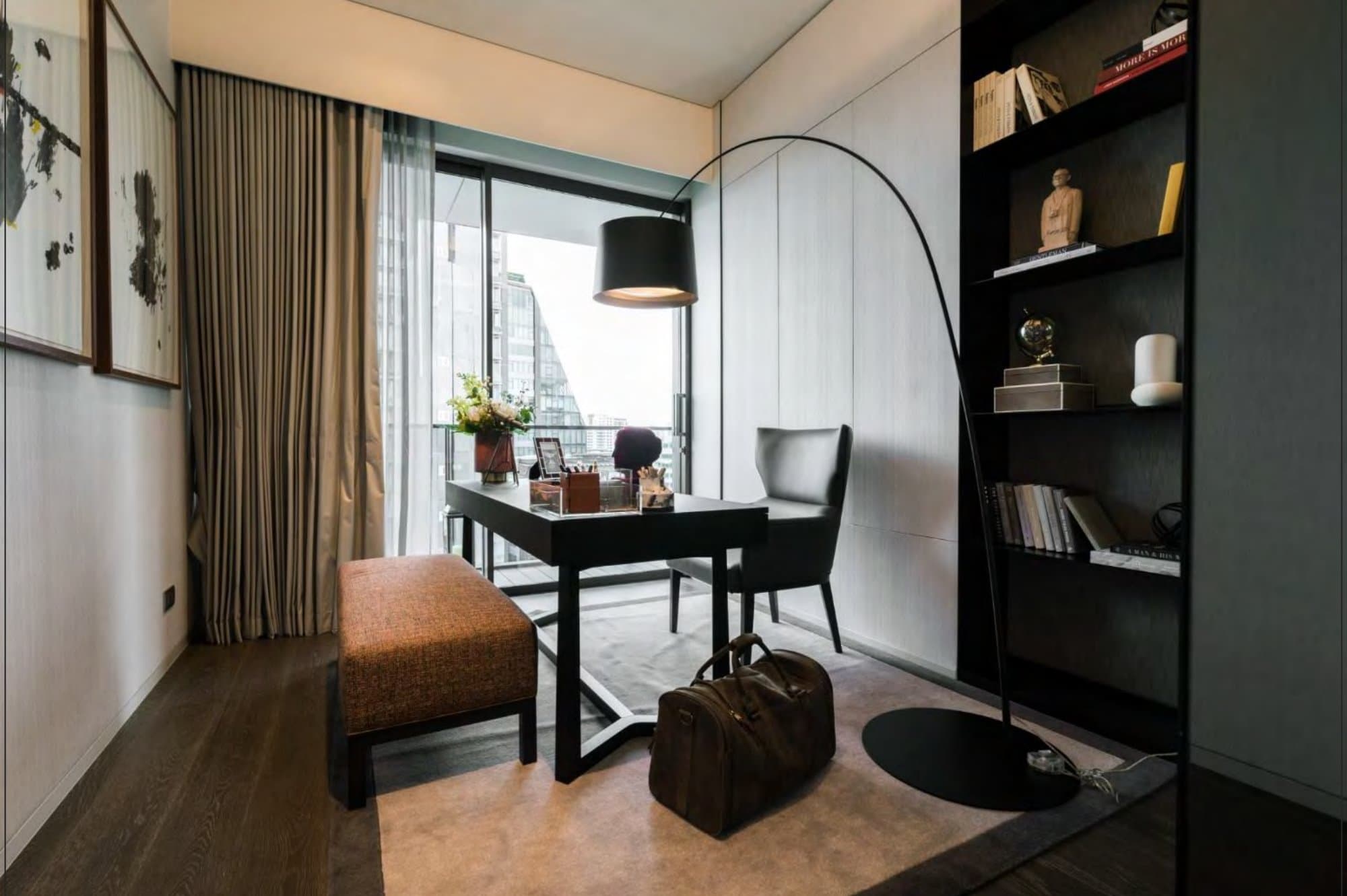 Study nook with a black writing desk, grey leather wingback, arched floor lamp and dark shelving, a leather holdall resting on the rug