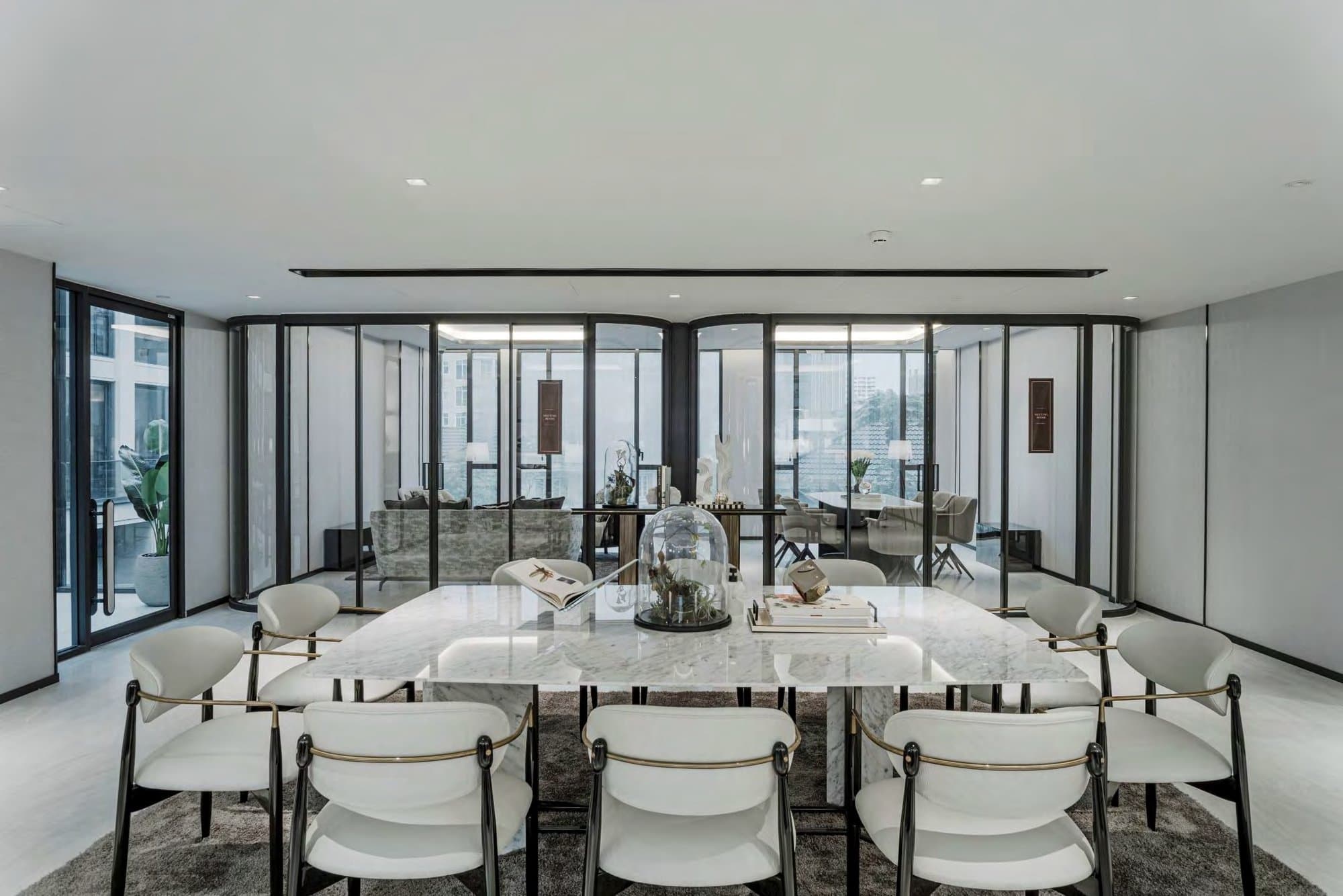 Function room centred on a white marble table ringed by brass-trimmed chairs, with curved glass partitions opening to lounges and city views.