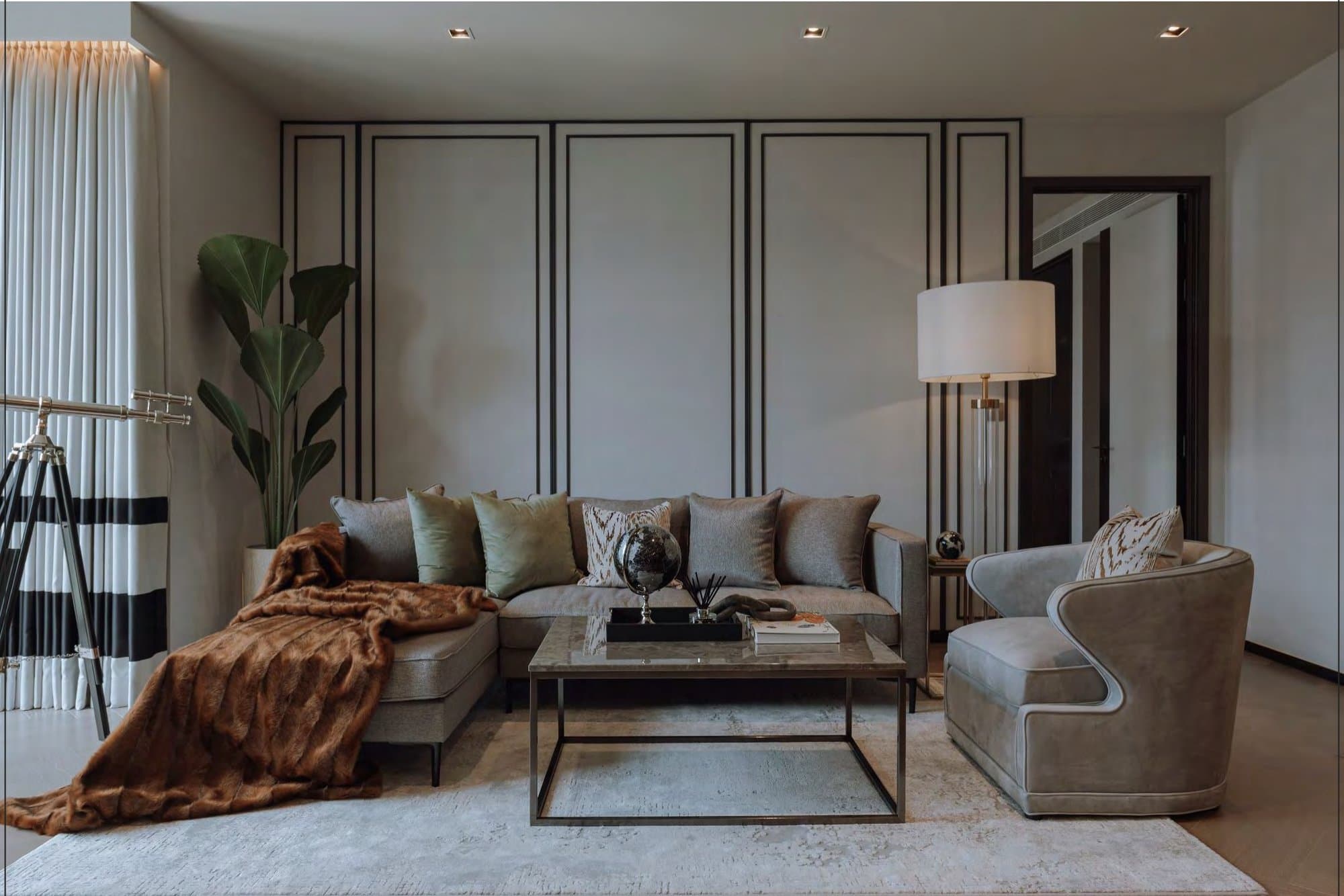 Show-unit living room with a grey sectional sofa, fur throw, panelled walls, marble coffee table and a velvet armchair under a floor lamp.