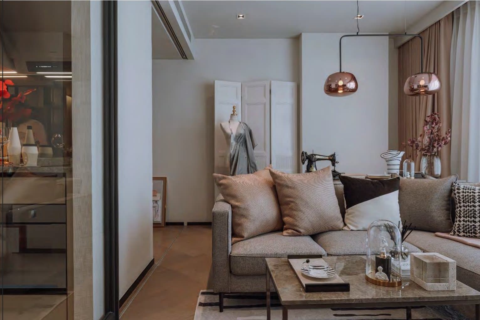 Sitting area with twin copper pendant lamps and a linen sofa in blush and taupe cushions, styled beside a vintage sewing machine and dress form.