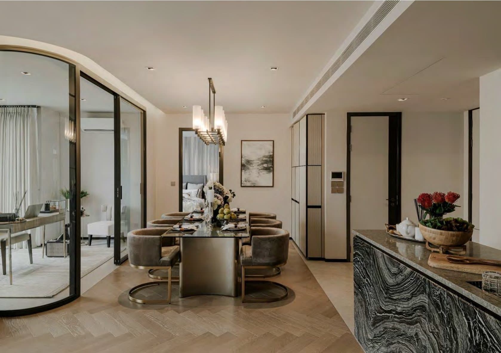 Dining area with a brass-based table and grey velvet chairs, a tiered pendant light, and a dramatic veined-marble waterfall console.