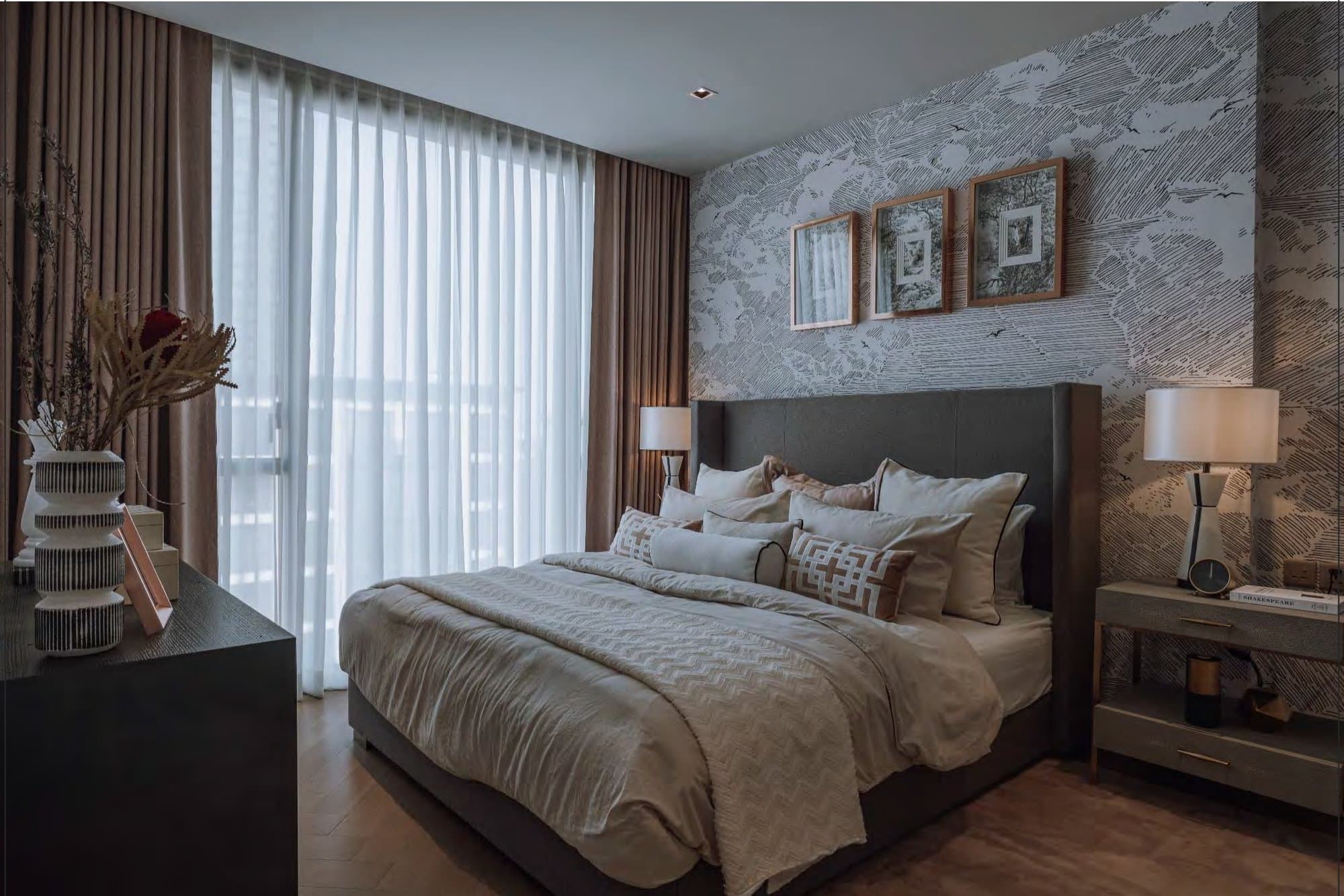 Bedroom framed by sketch-effect wallpaper and warm brown drapes, with twin table lamps, a dark headboard and layered neutral bedding.