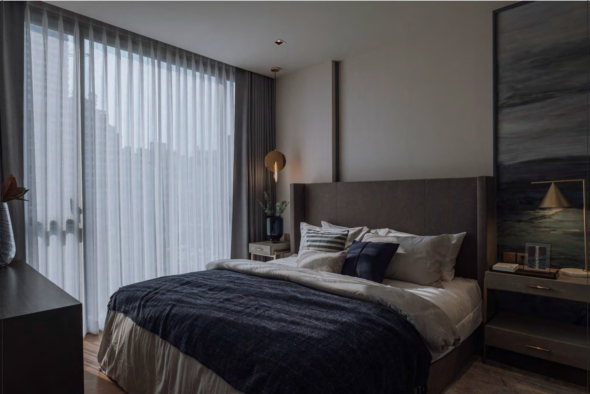 Masculine bedroom in charcoal and navy, with a dark throw, brass disc pendant, sheer curtains and a moody seascape canvas.