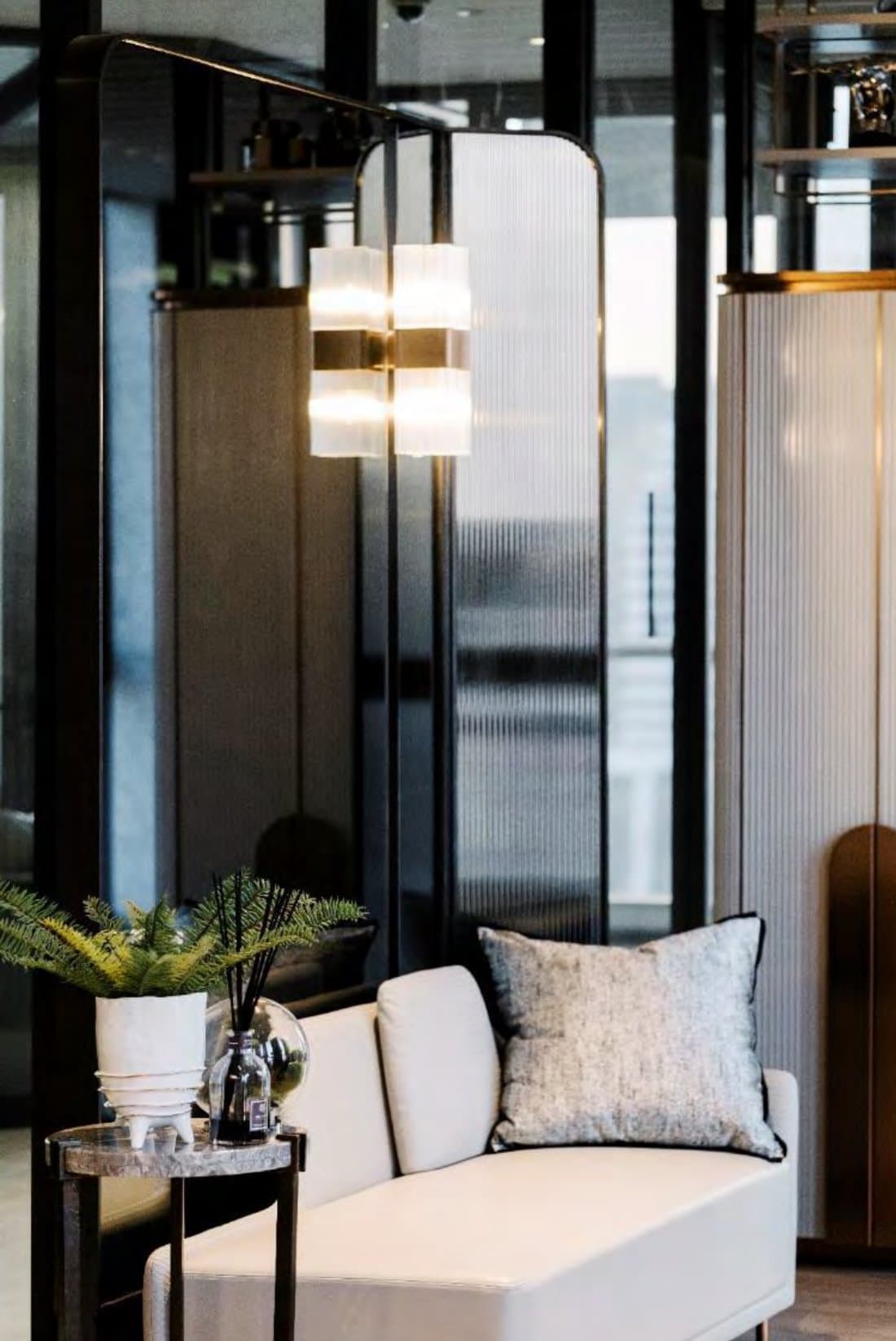 Quiet corner with a cream chaise, textured cushion, potted fern and a fluted-glass sconce against a reeded-glass screen