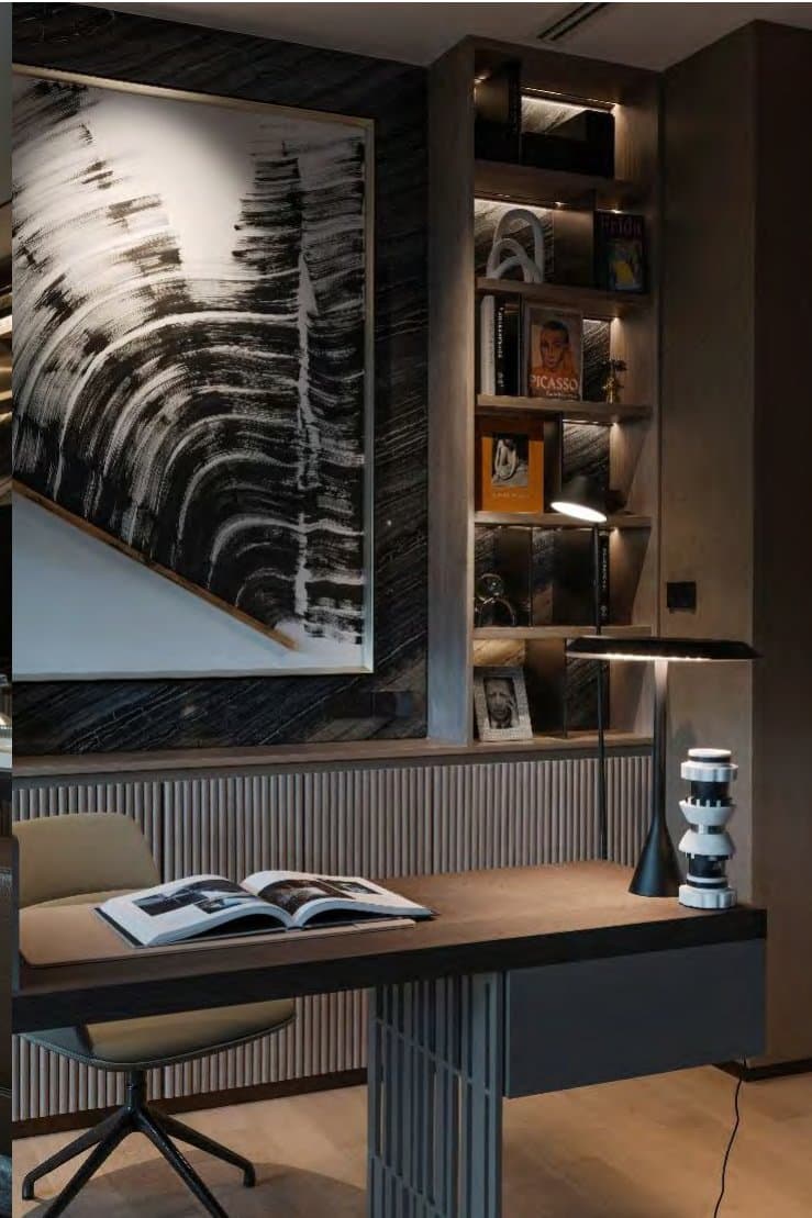 Study corner detail with framed monochrome brushstroke artwork above a fluted desk, shelved art books, task lamp and sculptural black lamp.