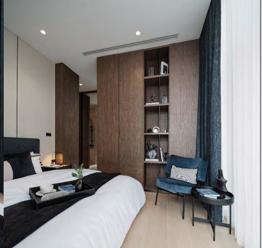 Bedroom with dark upholstered headboard, walnut wardrobes, glazed display niche, blue velvet chair and a breakfast tray on white linen.
