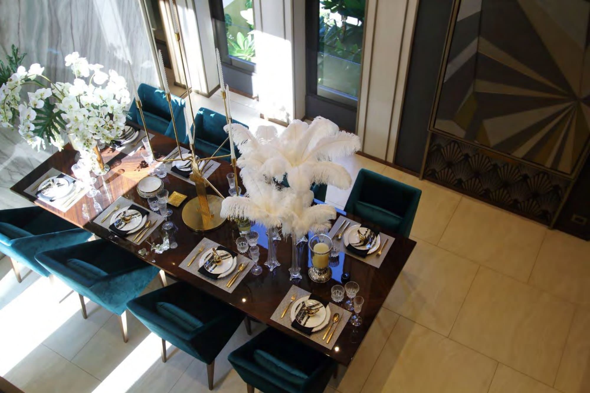 Overhead view of a dining table dressed with ostrich feathers, gold flatware and monochrome china beside an art-deco fan cabinet