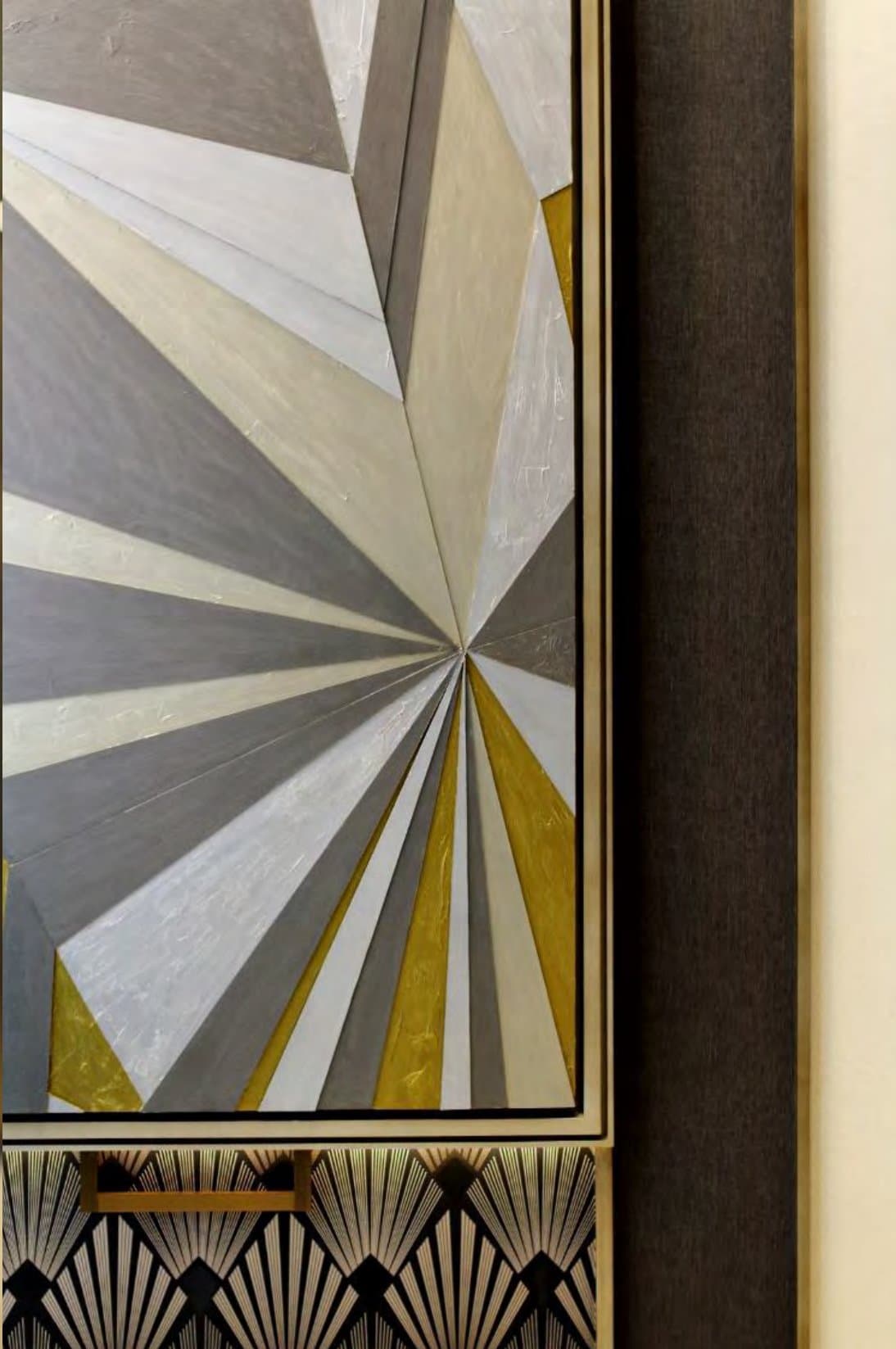 Framed art-deco wall panel of faceted grey, cream and gold-leaf rays set above a black-and-brass fan-patterned cabinet