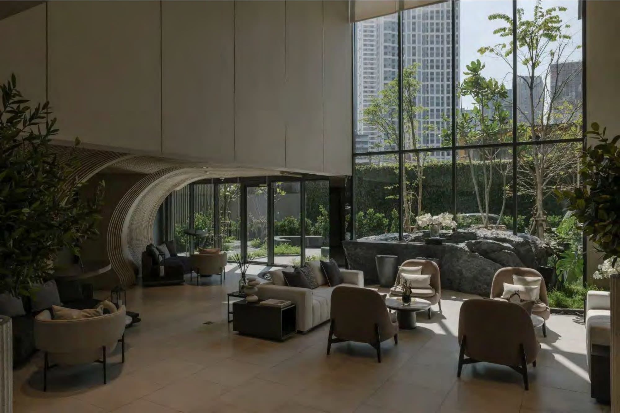 Double-height lounge with curved ribbed canopy, taupe armchairs and sofas, potted greenery, framing a garden of trees and distant city towers.