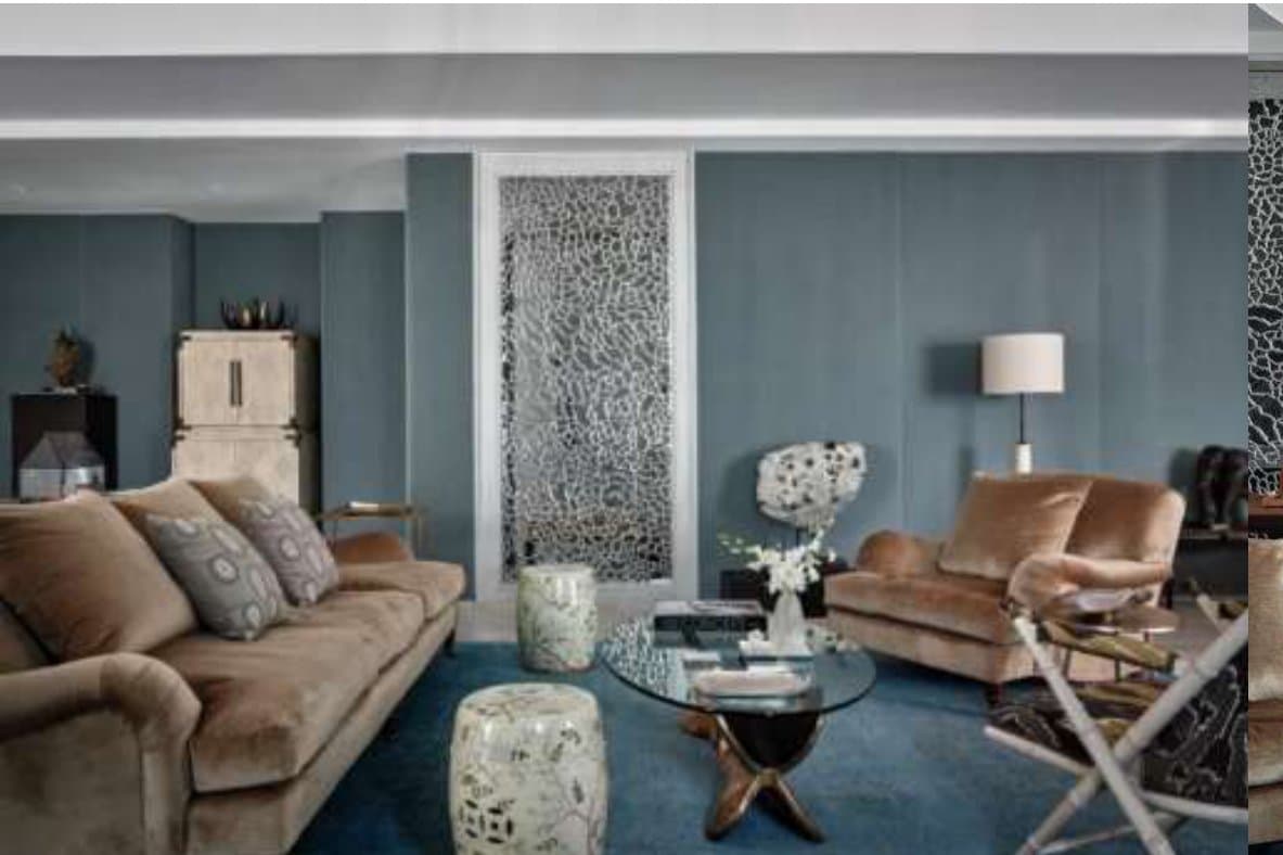 Living room in blue-grey velvet-panelled walls with a camel velvet sofa, glass-topped coffee table, ceramic garden stools and a filigree mirrored screen.