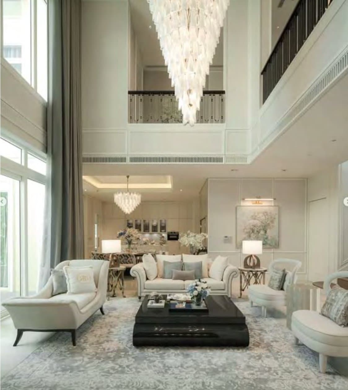 Double-height living room with a cascading white-petal chandelier, cream sofas and curved wing chairs around a black-lacquer table