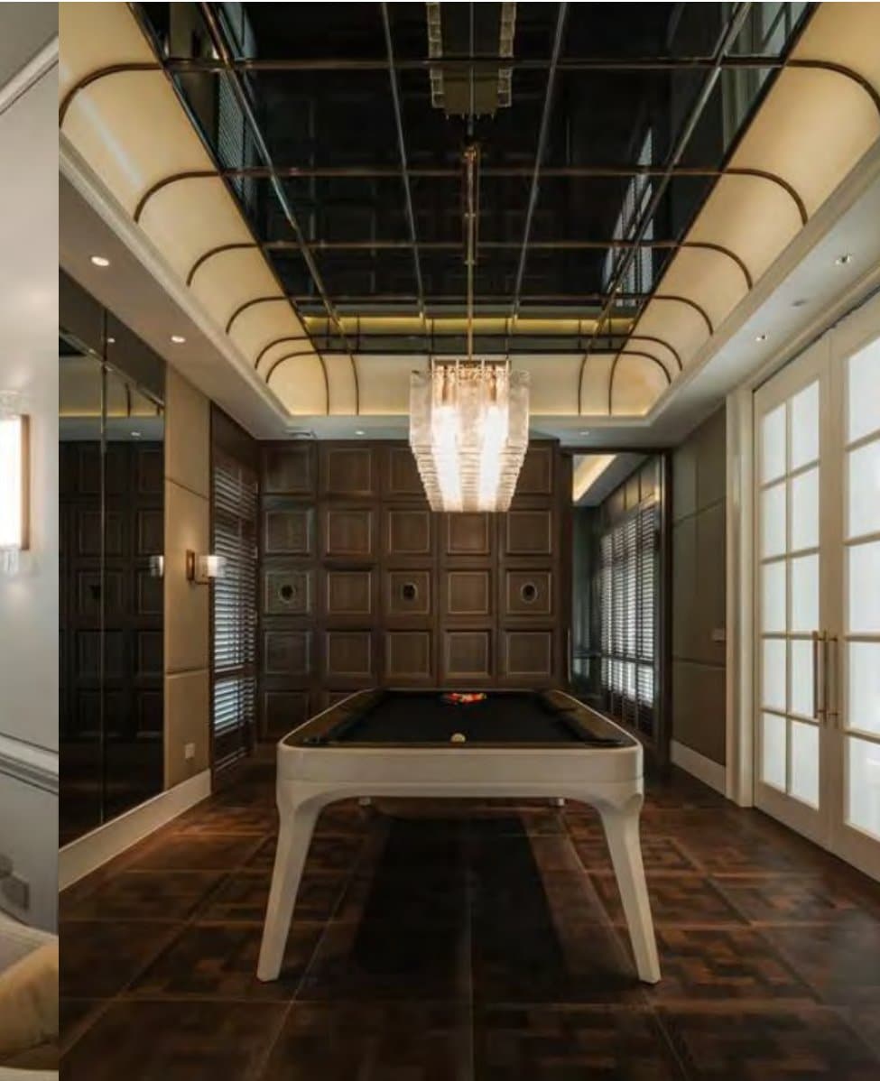 Games room with a white-based billiard table beneath a mirrored gold-lined ceiling, panelled walnut walls and a linear crystal chandelier