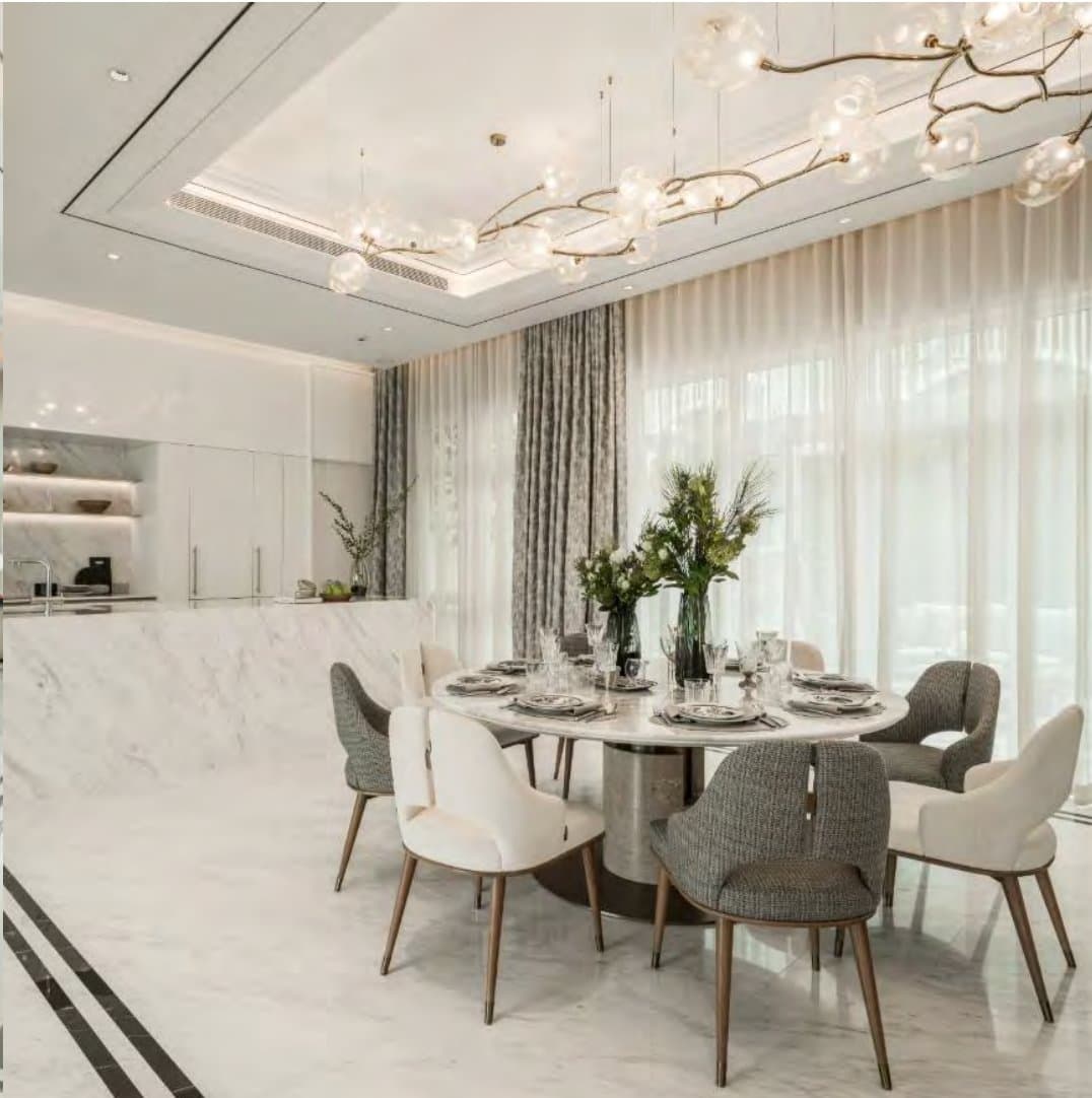 Bright breakfast room with a round marble table, cream and grey tweed chairs, a glass-bubble chandelier and a marble waterfall island behind