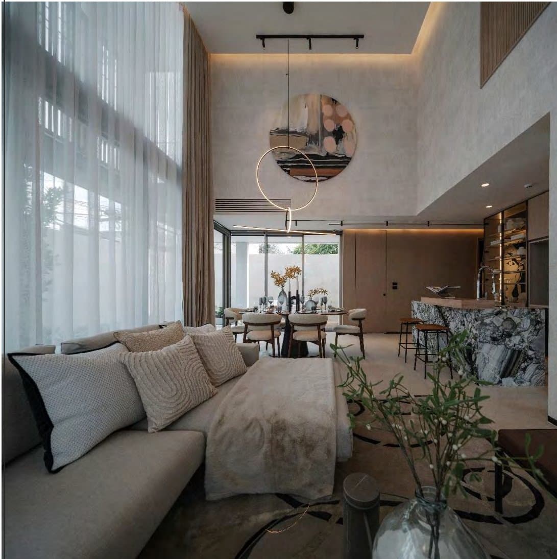 Double-height living room with pale boucle sectional, round abstract canvas, sculptural ring pendant and floor-to-ceiling sheers, marble bar beyond.